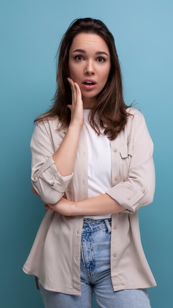 Verontruste brunette jaar oude vrouwelijke persoon gekleed in shirt en spijkerbroek camera kijken op blauw