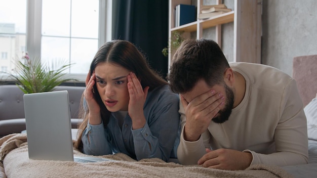 Verontwaardigd echtpaar teleurgesteld vrouw vrouw en man man blanke familie met laptop apparaat op bed kijk