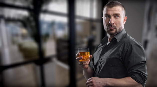 Verontwaardigde jonge man drinker alcoholist zit aan de bar met een glas whisky alleen te drinken