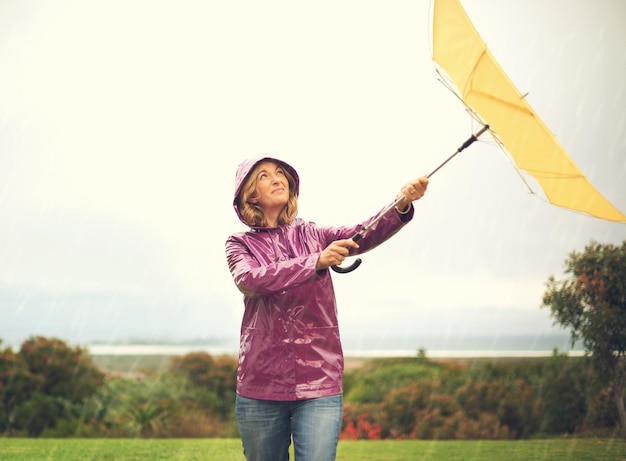 Verontwaardigde vrouw en paraplu met regenjas voor slecht weer en regenbui in het park in de natuur Vrouwelijke persoon regen en vechten met de wind voor dekking of bescherming in de buitenlucht in het winterseizoen in Glasgow