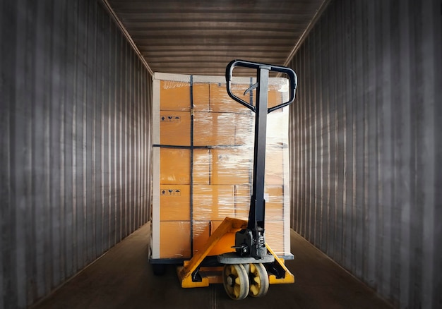 Verpakkingsdozen verpakt plastic gestapeld op pallet met handpallettruck. Binnen verzendcontainer