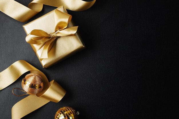 Verpakt gouden geschenk met gouden boog en kerstballen op donker.