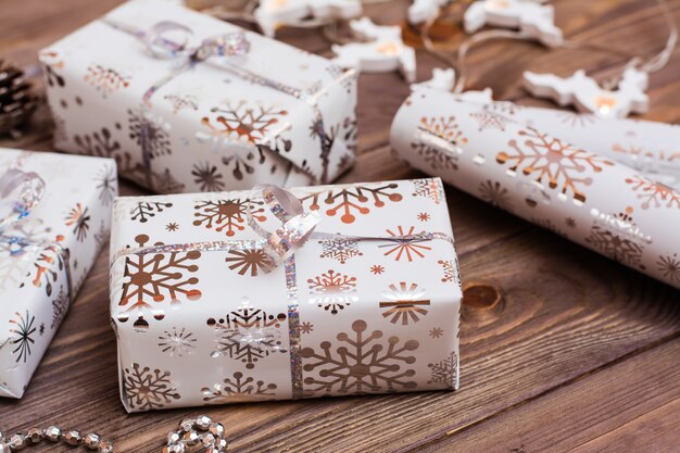 Foto verpakt in feestelijke verpakking geschenkdozen gebonden met zilveren lint en een rol inpakpapier op een houten tafel. kerstmis voorbereiden.