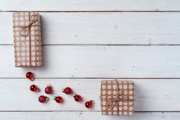 Verpakte kleine kerstcadeaus en rode kerstballen op wit houten bord bovenaanzicht