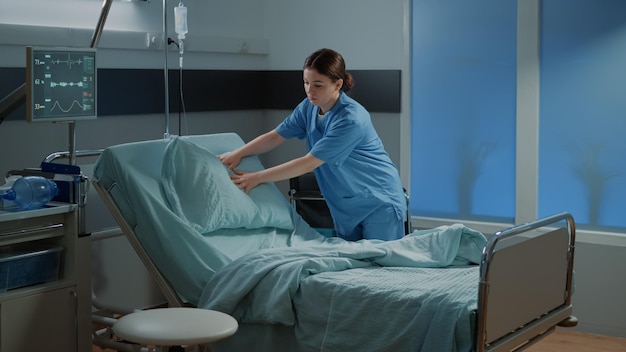 Verpleegkundige bed en deken in ziekenhuisafdeling voorbereiden voor patiënt. Klinische kamer met medische apparatuur, moderne technologie, monitor, rolstoel voor het genezen van ziekte, ziekte, chirurgie