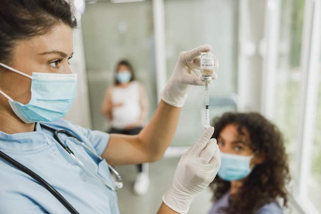 Verpleegkundige die de spuit vasthoudt en Covid-19-vaccinatie-injectiedosis maakt in de schouder van de patiënt.