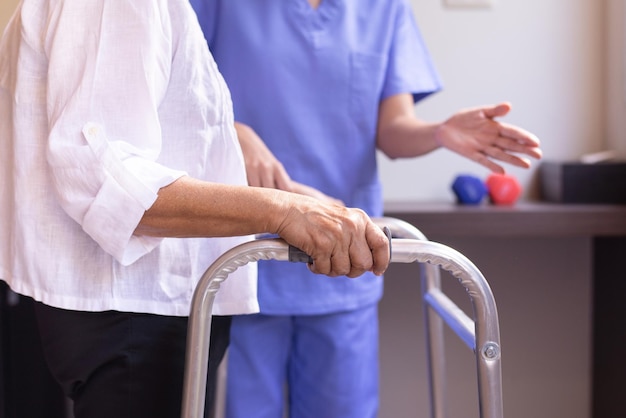Verpleegkundige helpt senior vrouw hand met rollator die probeert te lopen, zorg verpleeghuis concept