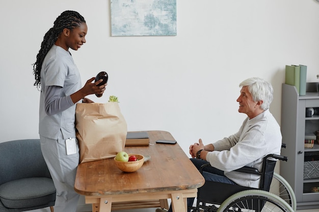Verpleegkundige levert tas met boodschappen aan senior man met een handicap