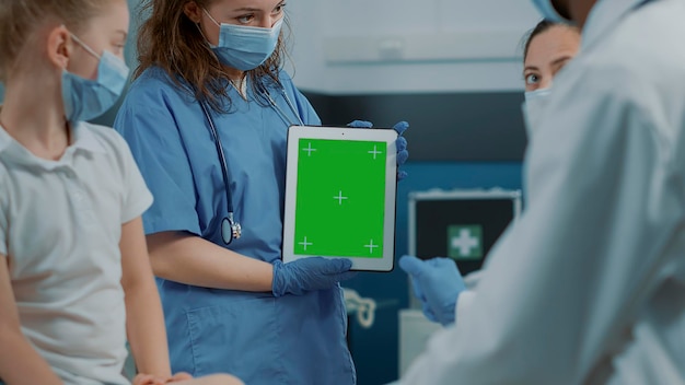 Verpleegkundige met digitale tablet met groen schermachtergrond bij controlebezoek. Medisch assistent die geïsoleerde kopieerruimte gebruikt met lege Chromakey en mockup-sjabloon op gadget tijdens pandemie.