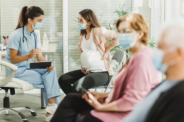 Verpleegkundige praat met jonge zwangere vrouw en maakt aantekeningen voor covid-19-vaccin in de wachtkamer van het ziekenhuis.