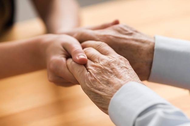 Verpleegster die de handen van de hogere man voor empathie houdt