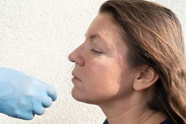 Verpleegster in blauwe handschoenen doet nasale corona-virustest bij vrouw