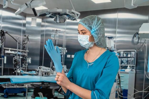 Verpleegster in jas trekt blauwe rubberen handschoenen aan en bereidt zich voor om een patiënt in de operatiekamer te onderzoeken