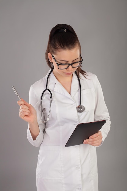 Verpleegster in wit gewaad en met bril schrijft iets in haar aantekeningen tegen een grijze achtergrond