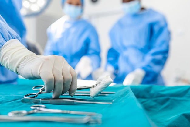 Verpleegster met de hand die chirurgisch instrument voor een groep chirurgen op de achtergrond opneemt patiënt in de operatiekamer Stalen medische instrumenten klaar voor gebruik Chirurgie en noodconcept