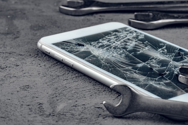 Verpletterde smartphone met reparatie tools op grijze achtergrond