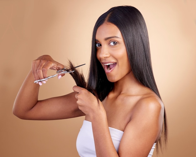 Verrassing knippen en portret van Indiase vrouw met schaar in studio voor doe-het-zelf kapsel of styling op bruine achtergrond Wow gezicht en vrouwelijk model met haarbehandeling of styling resultaten met schoonheidstool