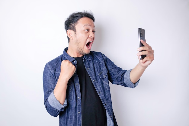 Verrast Aziatische man met marineblauw shirt wijzend op zijn smartphone geïsoleerd door witte achtergrond