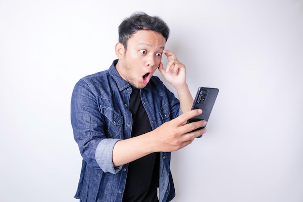 Verrast Aziatische man met marineblauw shirt wijzend op zijn smartphone geïsoleerd door witte achtergrond