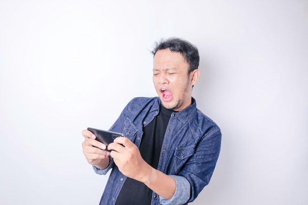 Verrast Aziatische man met marineblauw shirt wijzend op zijn smartphone geïsoleerd door witte achtergrond