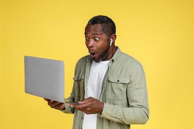 Verrast gelukkig grappige volwassen Afro-Amerikaanse man in casual en koptelefoon kijken naar laptop