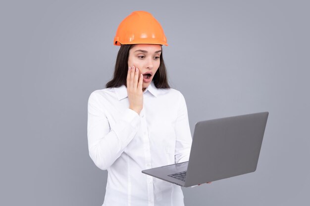 Verrast geschokt opgewonden zakenvrouw met laptopcomputer portret op grijs Portret van vrouwelijke bouwvakker in veiligheidshelm