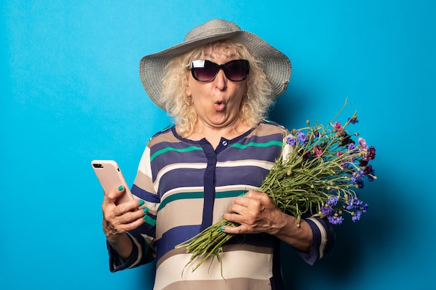 Foto verrast geschokt oude vrouw met een boeket bloemen met een telefoon