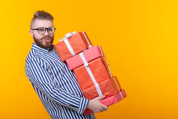 Verrast jonge hipster kerel in glazen met een grote stapel geschenkdozen op een gele ruimte