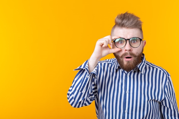 Verrast jonge hipster man met een snor en baard kijkt door een bril die zich voordeed op een geel