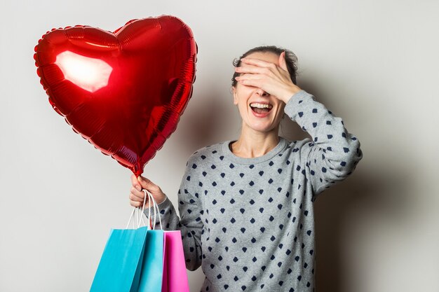 Verrast Jonge vrouw in een trui houdt een poarok voor en hart luchtballon en verheugt zich over het geschenk op een lichte achtergrond. Valentijnsdag concept. Banner.