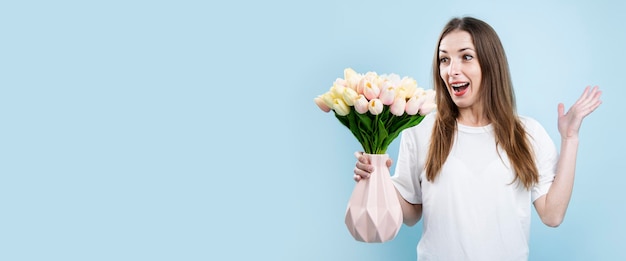 Verrast jonge vrouw met tulpen in vaas op blauwe achtergrond Banner