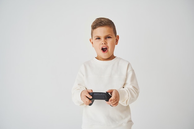 Verrast kind met gamepad die consolespellen speelt op witte achtergrond Gokverslaving van kind
