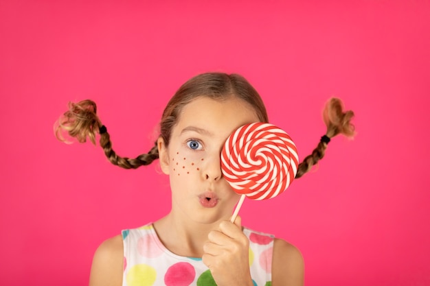 Verrast kind met vlechten die lolly houden Portret van buitensporig meisje tegen roze background