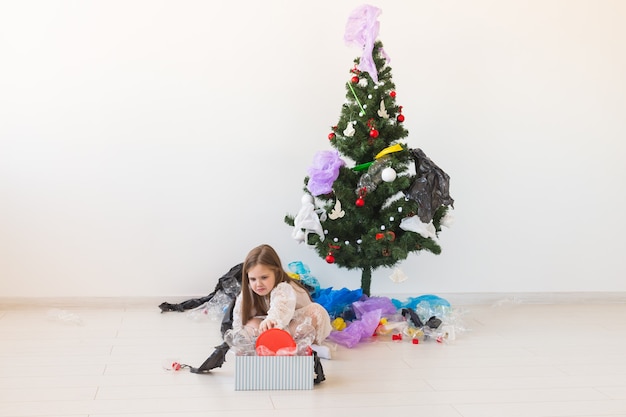 Verrast kinderdraagtas met plastic afval over de kerstboom