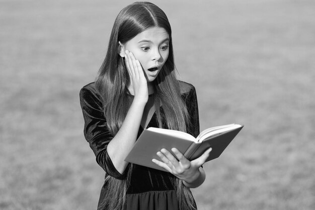 Verrast klein kind met open mond lees schoolboek groen gras zonnige zomer buiten informatie