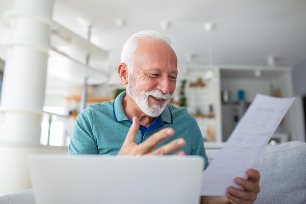 Verrast lachende gepensioneerde man onderzoekt vreugdevol een document dat financiële informatie analyseert Uit opwinding dat hij mogelijk een belastingteruggave of goedkeuring van een banklening heeft ontvangen om het succes vast te leggen