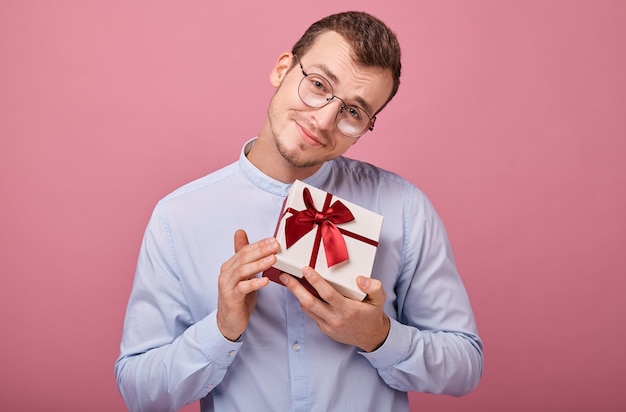 verrast man in shirt met bril houdt geschenk in doos met deksel en rode strik in zijn handen