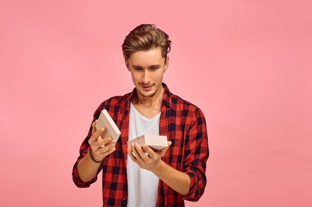 Verrast man opent geschenkdoos, roze muur, emotie. Gezichtsuitdrukking, mannelijke persoon op zoek op camera in studio, emotioneel concept, gevoelens