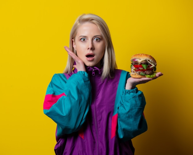 Verrast meisje in 80s kledingstijl met hamburger op gele ruimte
