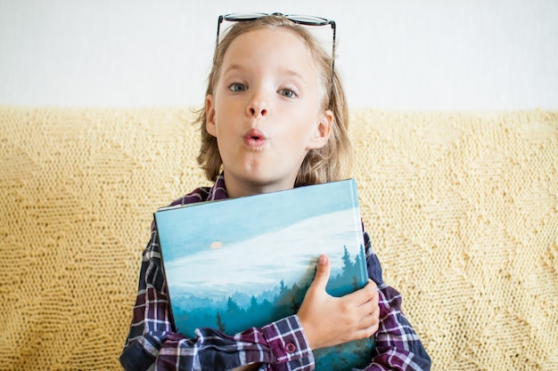 Verrast meisje in een geruit hemd en bril houdt een stapel boeken in haar handen online leren