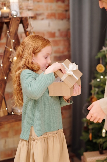 Verrast meisje in vrijetijdskleding geschenkdoos openen met kerstcadeau van haar moeder