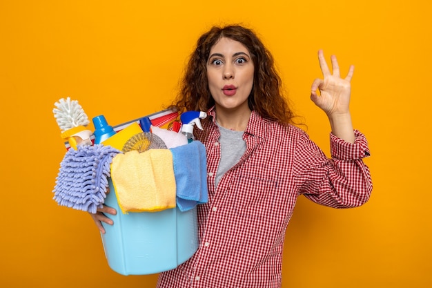 Verrast met goed gebaar jonge schoonmaakster met emmer schoonmaakgereedschap