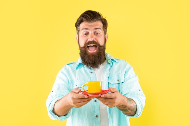 Verrast ongeschoren man in shirt met koffie op gele achtergrond cappuccino