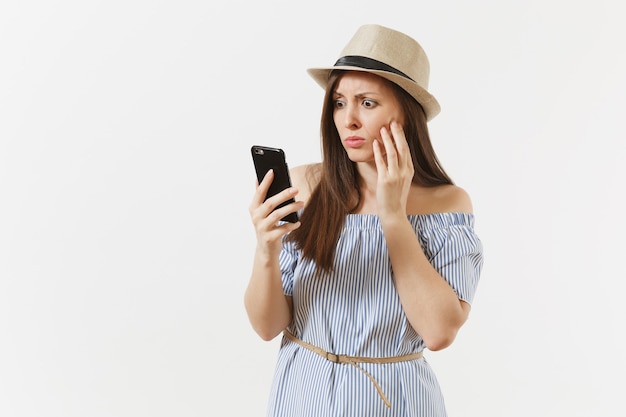 Verrast overstuur jonge vrouw gekleed blauwe jurk, hoed heeft wat problemen, hoort nepnieuws of onverwacht gerucht in mobiele telefoon geïsoleerd op een witte achtergrond. mensen, oprechte emoties, lifestyle concept.