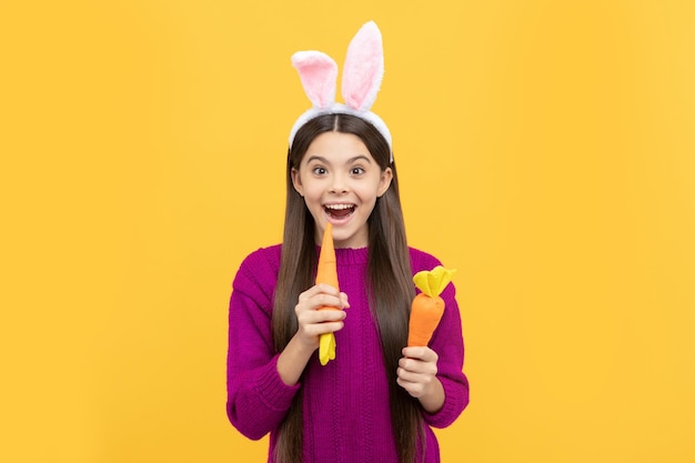 Verrast paastienermeisje in grappige konijnenoren bijt wortel vrolijk pasen