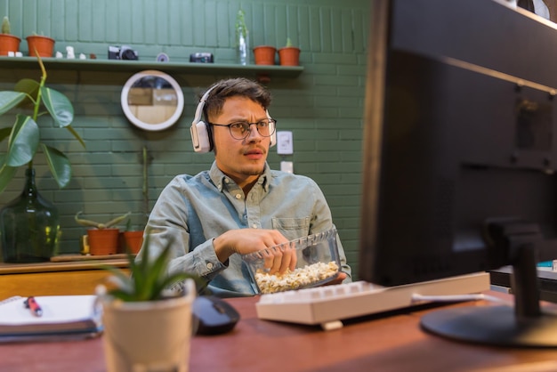 Verrast Spaans mannetje dat met koptelefoon popcorn achter de computer eet