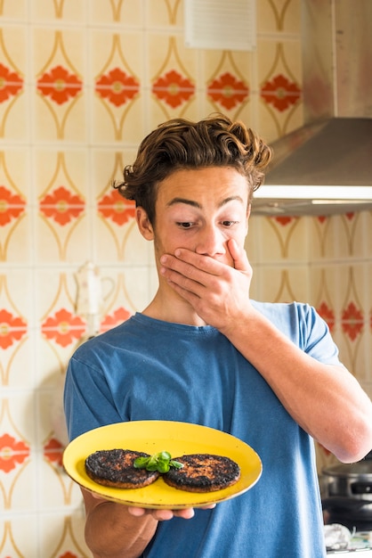 Foto verrast tiener na brned twee hamburgers gekookt in de keuken thuis