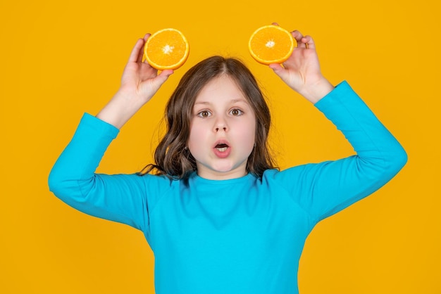 Verrast tienermeisje houdt oranje fruit op gele achtergrond