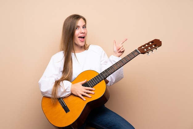 Verrast tienermeisje met gitaar en wijzende vinger aan de kant