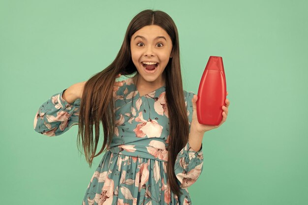 Verrast tienermeisje met lang haar houdt shampoofles haarbehandeling vast